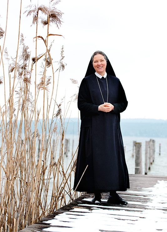 Ordensschwester in Tracht steht auf Steg und lächelt glücklich - das Glück ü50
